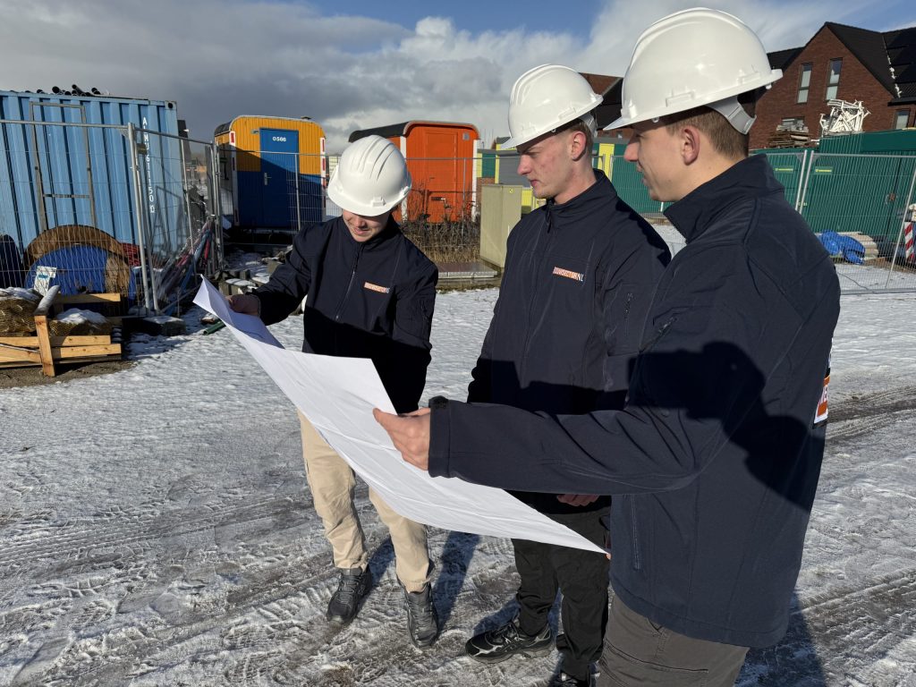Drie vakmensen van Bouwsector Nederland met witte helm bekijken samen een bouwtekening